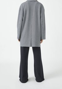Abrigo de cuadros en gris y blanco con un corte ajustado, mangas largas y solapa, combinado con pantalones anchos oscuros.