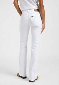 Jeans acampanados blancos con bolsillos delanteros y traseros, que presentan una etiqueta de cuero en la cinturilla. Textura suave con una silueta ajustada.