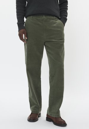 Kakis Corduroyhose mit geradem Schnitt, strukturierter Stoff und Seitentaschen, kombiniert mit braunen Stiefeln und einem dunklen Pullover.