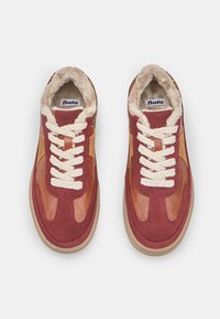 Červené a hnedé tenisky s kožušinovou podšívkou. Obsahujú okrúhle šnúrky, textúrovanú gumovú podošvu a kontrastné panely z semišu a kože.