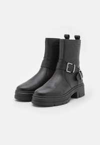 Melnas ādas potītes zābaki ar teksturētu apdari, apaļu purngalu un plašu blokveida papēdi. Satur sprādzes jostu akcentu sānos.