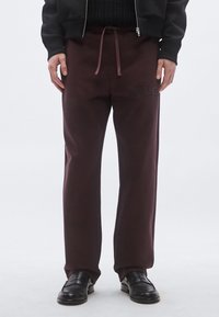 Pantaloni de trening burgundy cu talie ajustabilă cu șnur, având o aplicație cu logo texturat. Realizați dintr-un material moale, cu croială lejeră.