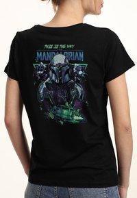 Svart bomull t-shirt med en grafisk design av en Mandalorian-hjälm, med texten "DETTA ÄR VÄGEN" i blått och grönt, samt stjärnaccent.