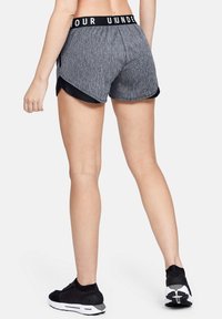 Grå sportshorts med svart midjeband, med en överlappande design och sidofickor. I kombination med svarta sneakers.