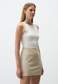 Witte geribde tanktop gecombineerd met een beige minirok met verticale witte strepen. Glad textuur zonder zichtbare hardware of accenten.