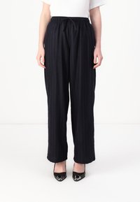 Navy pinstriped trousers with an elastic waistband, relaxed fit, and side pockets, paired with black pointed-toe shoes.