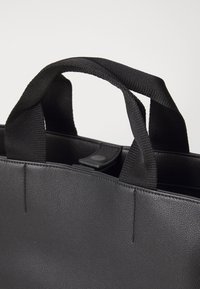 Borsa tote nera con finitura testurizzata, dotata di robuste maniglie in tessuto e chiusura a scatto nella parte superiore. Design minimalista, forma rettangolare.
