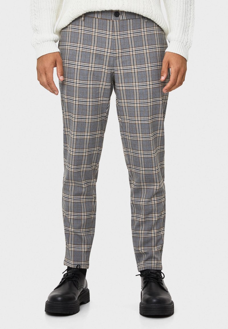 Gray plaid trousers with a fitted cut, featuring white and tan lines. Made from a textured fabric, paired with black lace-up shoes.