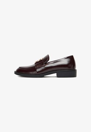 Burgundowe skórzane loafersy o eleganckim designie, z dekoracyjnym paskiem i przeszyciami. Podeszwa jest czarna i lekko teksturowana dla lepszej przyczepności.