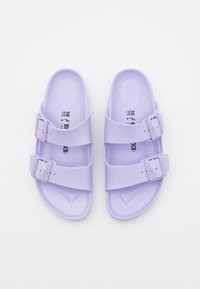Purple sandals made of smooth material, featuring two adjustable straps with buckles. The sole has a slight texture and footbed curve.