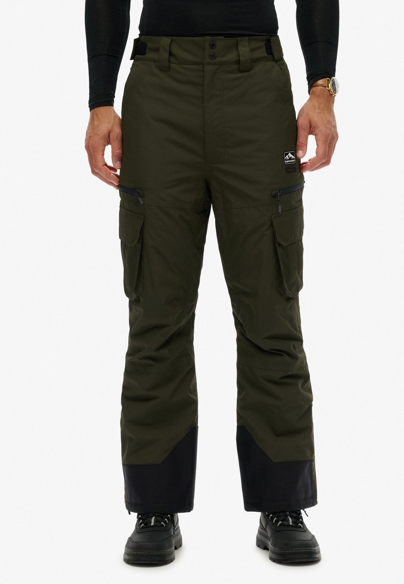 Cargo ski- of sneeuwbroek in donker olijfgroen, gemaakt van waterdicht materiaal. Voorzien van zakken, ritsen en een contrasterend zwart paneel aan de zoom.