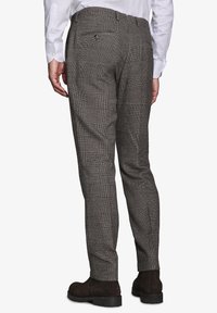 Mand iført brune ternede slim-fit bukser, hvid knap-agtig skjorte og mørkebrune ruskind støvler, vist fra ryggen.