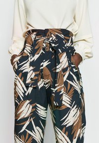 Blommönstrade byxor i marinblått med bruna och vita blad, med hög midja, knytbälte och sidofickor.