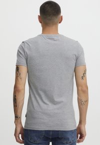 Tricou gri din bumbac, cu mâneci scurte, guler rotund, design ajustat și cusături vizibile. Prezintă tatuaje pe ambele brațe.
