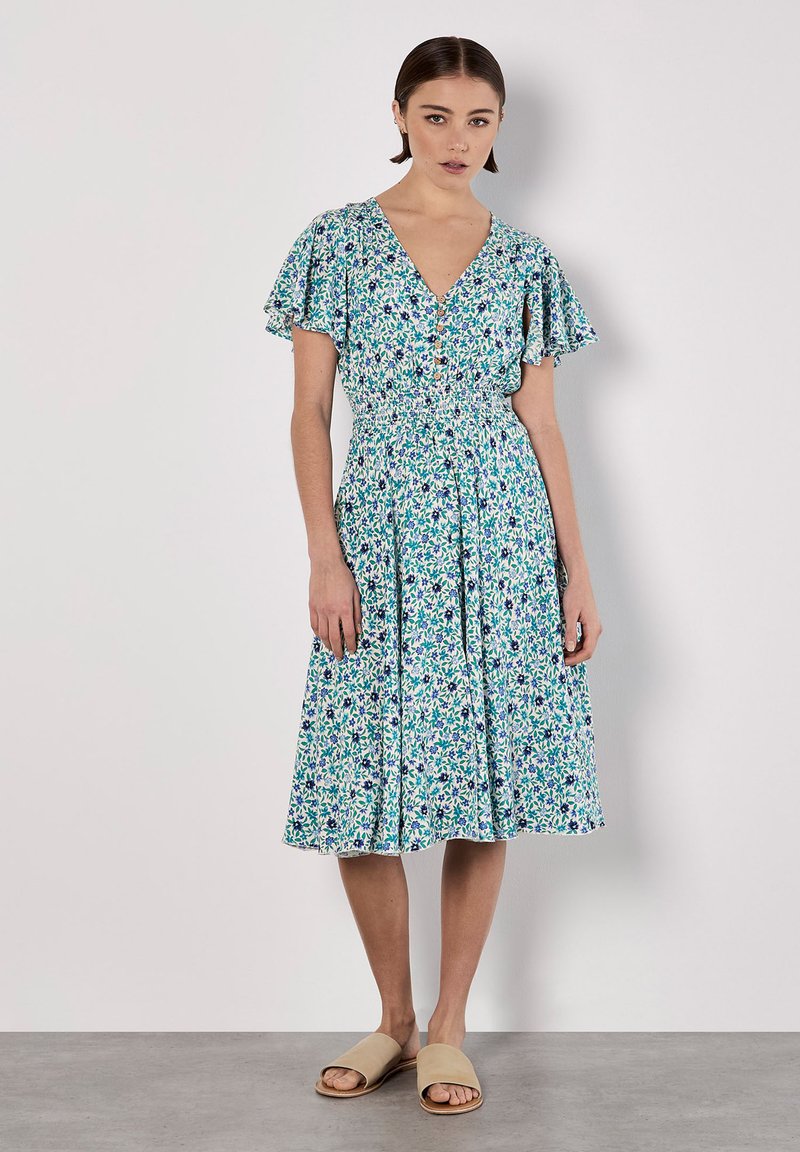 Blumenmuster-Kleid mit V-Ausschnitt, kurzen Rüschensäumen und tailliertem Bund. Die Farben umfassen Blau, Grün und Weiß mit einem fließenden Stoff.