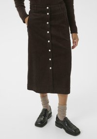 Brown corduroy midi skirt with front buttons, two side pockets, and a straight cut. Paired with black loafers and ribbed beige socks.