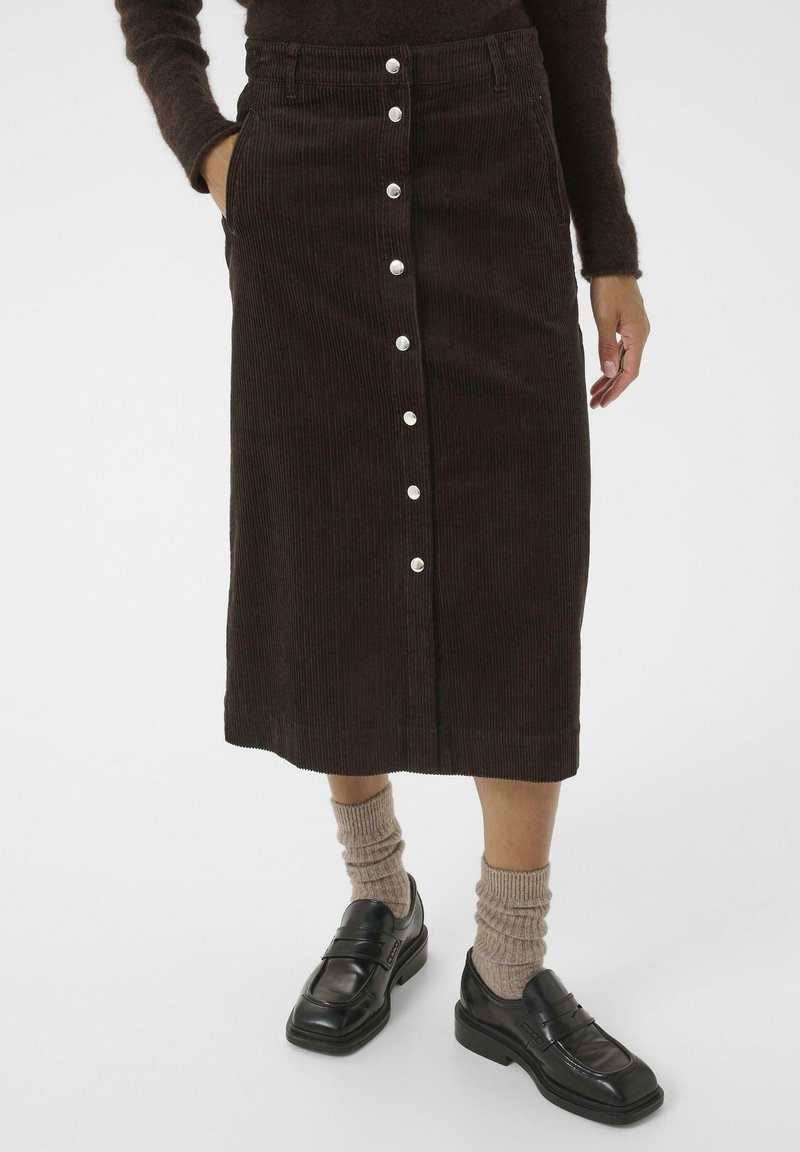 Brown corduroy midi skirt with front buttons, two side pockets, and a straight cut. Paired with black loafers and ribbed beige socks.