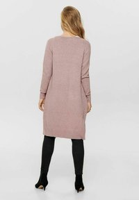 Abito a maglia rosa chiaro con maniche lunghe, polsini e orlo a coste, caratterizzato da una vestibilità dritta e fessure laterali. Abbinato a leggings neri e stivaletti.