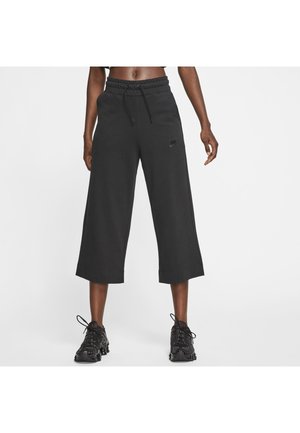 Pantalons de survêtement noirs coupés avec taille élastique et cordon de serrage, arborant un logo Nike discret sur le côté gauche. Texture lisse, coupe décontractée.