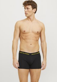 Schwarze Boxershorts aus elastischem Stoff mit einem gelben Logo-Bund. Sie verfügen über ein körpernahes Design und eine Länge bis zur Mitte des Oberschenkels mit flachen Nähten.