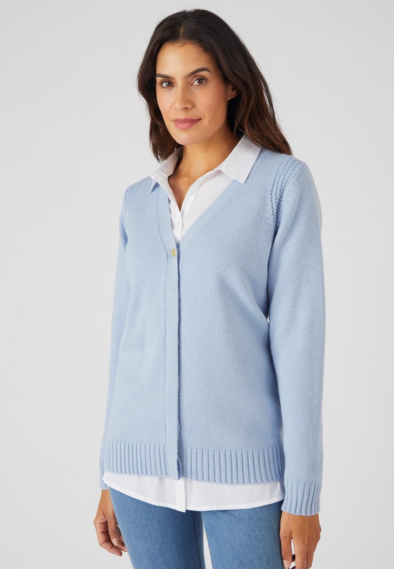 Cardigan en tricot bleu clair avec un col en V, ourlet et poignets côtelés, détail d'un seul bouton doré, porté sur une chemise blanche à col.