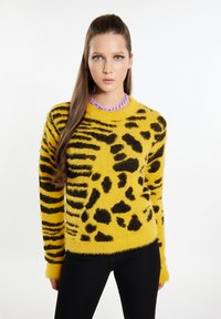 Geel harig sweater met zwarte tijgerstrepen en vlekken. Lange mouwen met ribgebreide manchetten, ronde hals en zachte textuur.