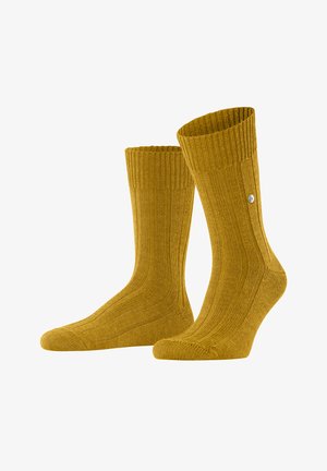 Calzini a coste giallo senape realizzati in un tessuto a maglia testurizzato, con un bordo superiore e un piccolo dettaglio del logo di lato.