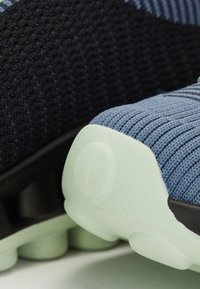 Sportliche Schuhe mit einem gestrickten Obermaterial in Dunkelblau und Hellblau, einer strukturierten mintgrünen Laufsohle und schwarzen Akzenten.