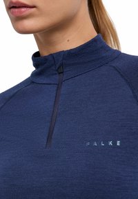 Granatowa bluza z długim rękawem, wysokim kołnierzem, półzamkiem i raglanowymi rękawami; na piersi logo "FALKE" w kolorze odblaskowym. Gładka faktura.