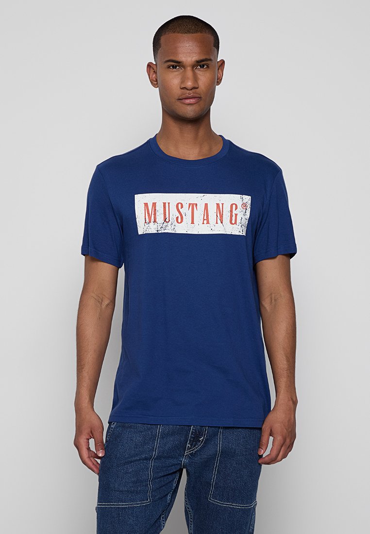 Marineblaue Baumwoll-T-Shirt mit rundem Halsausschnitt, ausgestattet mit einem weißen rechteckigen Grafikdesign, auf dem "MUSTANG" in fettem roten Text steht. Lässiges Design.