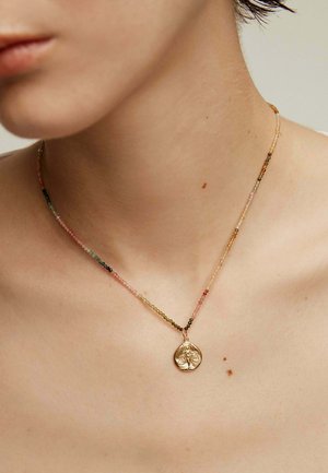 Collar de múltiples hilos que presenta pequeñas cuentas de colores en rosa, verde y negro, con un colgante dorado que muestra un diseño floral.