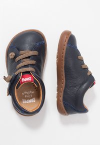 Scarpe in pelle blu navy con suola in gomma marrone. Le caratteristiche includono lacci marroni, cuciture a contrasto e un anello sul tallone per agevolare l'indossamento.