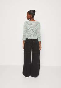 Minzgrüner, gestrickter, verkürzter Pullover mit gezacktem Saum und V-Muster. Kombiniert mit schwarzen, weiten Cargohosen mit Taschen.