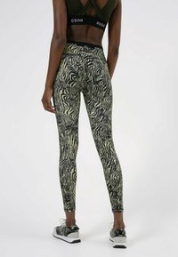 Leggings neri e crema con un motivo, realizzati in tessuto elastico, con una vita alta e una vestibilità aderente, abbinati a scarpe da ginnastica con motivo.