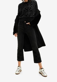 Czarny skrócony sweter z tłoczonym napisem, zestawiony z wysokim stanem czarnych dżinsów z kwiatowym wzorem na nogawkach. Całość dopełniają srebrne sneakersy.