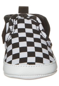 Zapato slip-on a rayas blancas y negras con suela blanca y tira negra en la parte trasera, visto desde el frente.