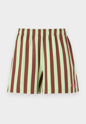 Person trägt ein übergroßes hellgrünes T-Shirt mit buntem Blumenmuster, gestreifte rote und beige Shorts, weiße Socken und rote Schnürstiefel.