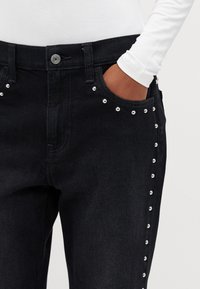 Jeans negri din denim cu nituri argintii de-a lungul cusăturii laterale. Prezintă un brâu clasic și buzunare frontale. Design și textură atemporale.