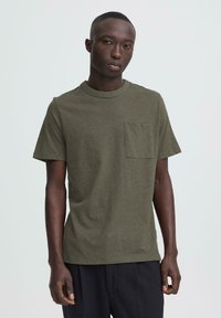 Maslinasto zelena kratka majica s okruglim izrezom i džepom na prsa, izrađena od mekane tkanine s glatkom teksturom.