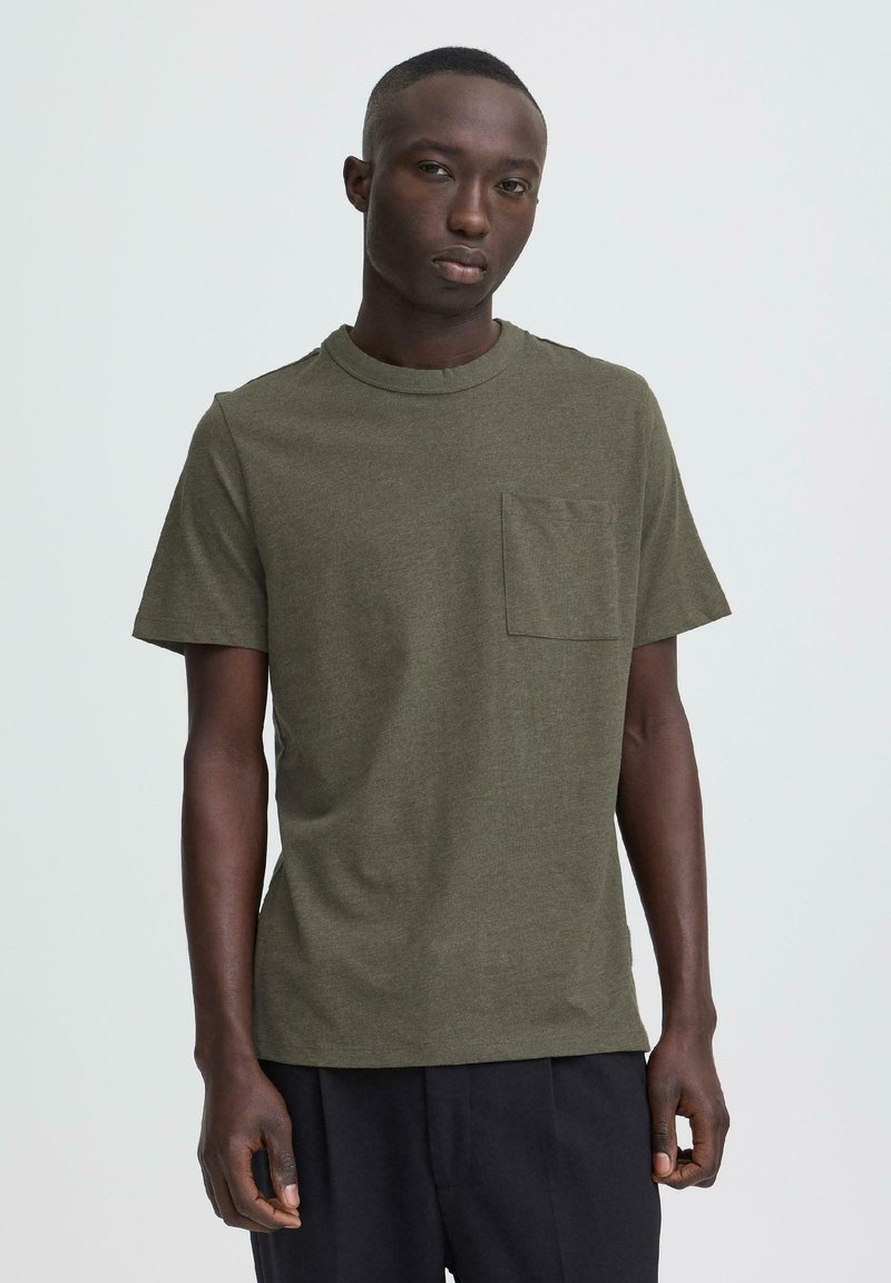 Olivengrønn t-skjorte med korte ermer, rund hals og brystlomme, laget av mykt stoff med en glatt tekstur.