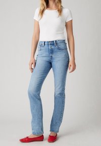 Ljusblå denimjeans med rak bendesign, hög midja och subtil blekning. Matchas med en åtsittande vit t-shirt och röda lägenheter.