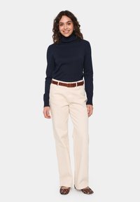 Navy turtleneck sweater, cream straight-leg trousers, brown belt, and black leopard-print flats. Smooth textures, casual fit.
