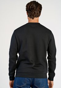 Felpa nera con scollo a girocollo, polsini e orlo a coste. Realizzata in un tessuto strutturato, abbinata a jeans in denim blu.