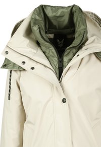Crème waterdichte jas met een verwijderbare olijfgroene binnenlaag. Kenmerken zijn een hoge kraag, ritssluitingen en drukknoopsluitingen, en een verstelbare capuchon.
