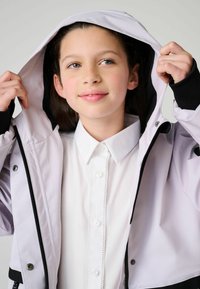 Svetlofialová bunda na zips s kapucňou, čierne akcenty a hladká textúra, oblečená na bielu košeľu s gombíkmi a dekoratívnym okrajom.