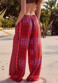 Pantalon large à motif rouge présentant une variété de dessins, y compris des rayures, des fleurs et des pois. Taille élastique avec poches latérales.