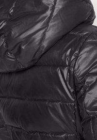 Svart puffjacka med en glänsande, slät yta, quiltat mönster med horisontella sektioner och en huva.