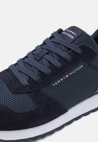 Tumesinine spordijalats, milles on segatud võrkkangas ja samet, esitleb tekstureeritud pinda, ümmargusi paelu ning logo keeltes.