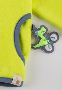 Fluorescent yellow fleece clothing with gray trim and a dinosaur bicycle tag featuring a green dinosaur character with a blue cap.