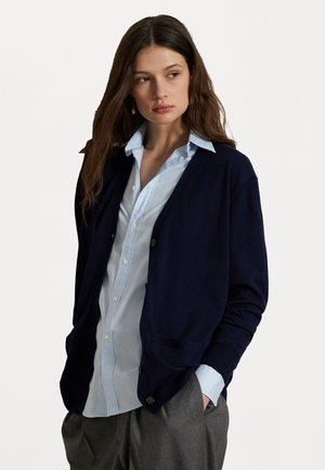 Navy cardigan made of soft fabric, featuring a relaxed fit, front pockets, and button closures, layered over a light blue button-up shirt.